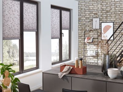 Moderne Wohnküche mit zwei Fenstern, dekorativen Rollos, einer Steinwand und einem Tisch mit Stühlen. Pflanzen und Deko-Elemente sind sichtbar.